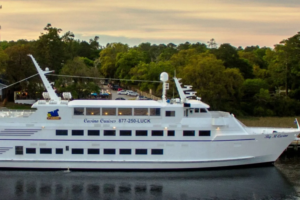 A striking exterior showing a luxurious cruise ship with casino branding, surrounded by greenery. The mood is lively and upscale, hinting at entertainment, dining, and social excitement that await nearby.