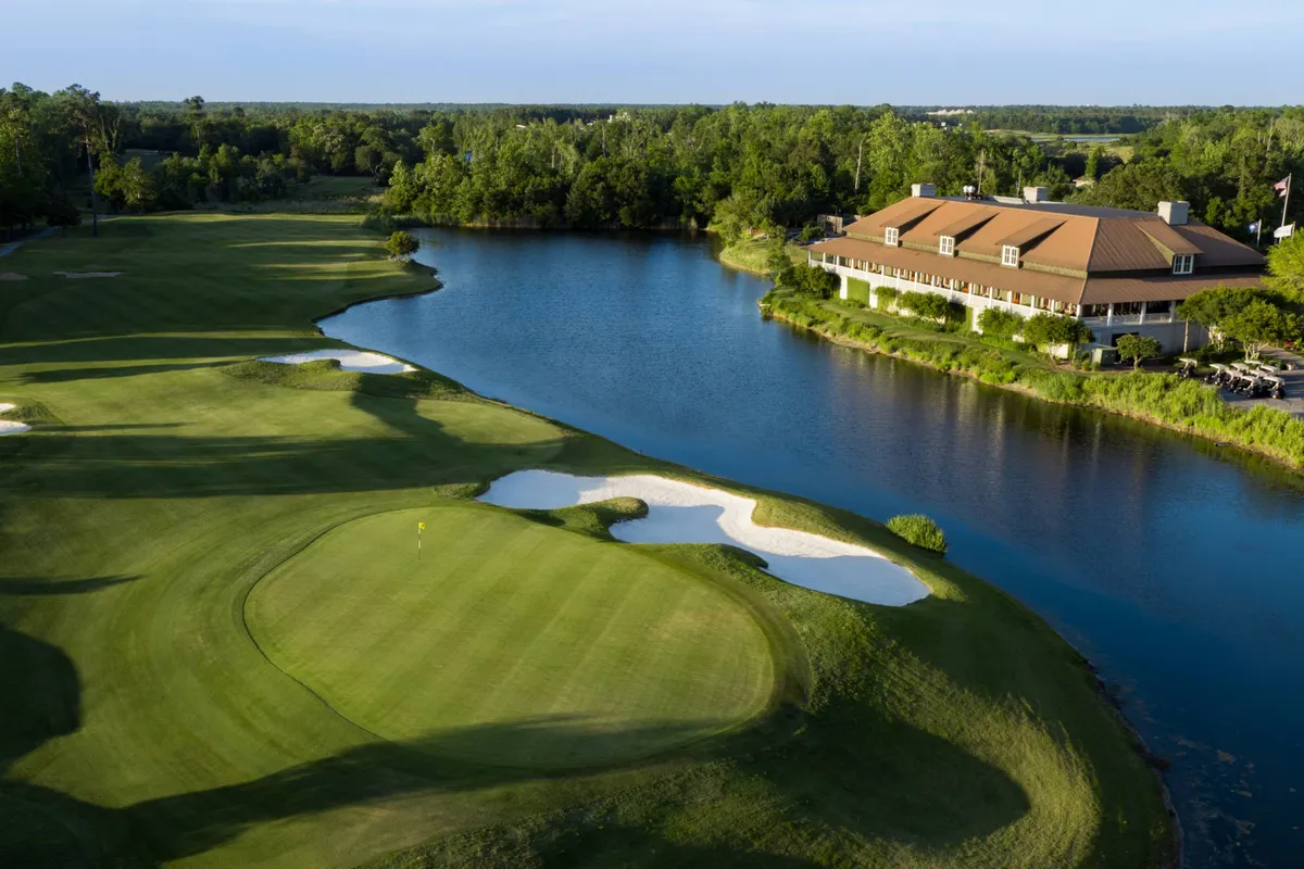 A sweeping view of a lush golf course featuring manicured greens, a tranquil lake, a prominent clubhouse in the distance, and visible sand traps. The scene is lively and inviting, evoking a sense of recreational possibility and relaxation.