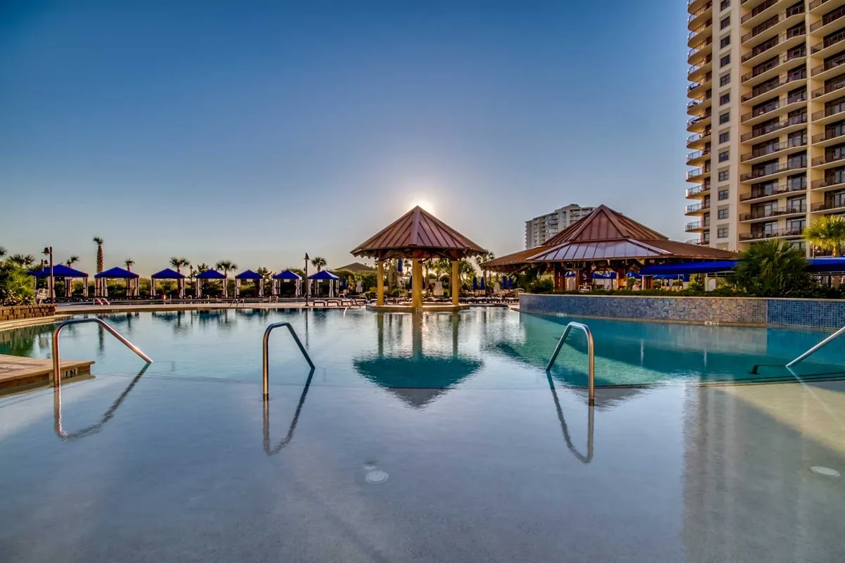 A tranquil outdoor pool area at sunset, with lounge chairs, pavilions, and a serene atmosphere ideal for relaxation and socializing.