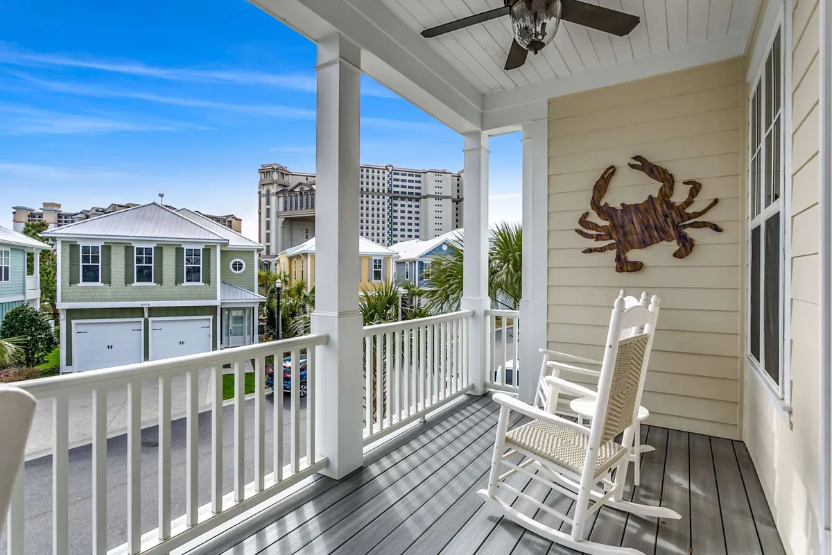 This image showcases a welcoming balcony with a rocking chair, decorative crab wall art, sturdy balcony railing, and views of surrounding homes. The balcony looks elevated, providing a tranquil spot for relaxation and enjoying the outdoors.