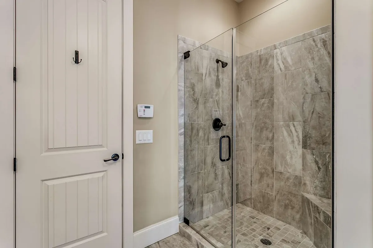 A modern bathroom with a glass shower enclosure, elegant marble tiles, and a sturdy door with a convenient hook. The atmosphere is clean and serene, offering guests an invigorating shower and a quiet moment to themselves.