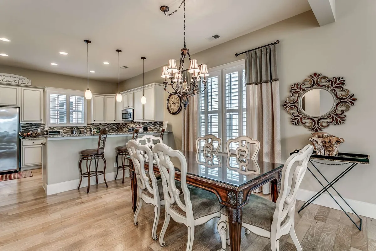 An inviting open-plan space featuring a stylish dining table beneath a chandelier, a spacious kitchen island, and a large mirror that reflects natural light throughout the area. This room is designed for shared meals and lively conversation, seamlessly connecting kitchen and dining in a sophisticated ambiance.