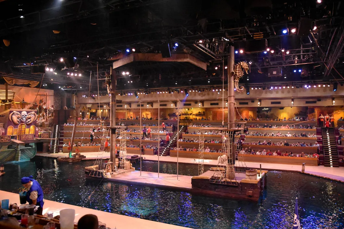 An exciting, themed performance venue interior featuring large ship props, a water stage, and lively audience seating, capturing the thrill of live entertainment.