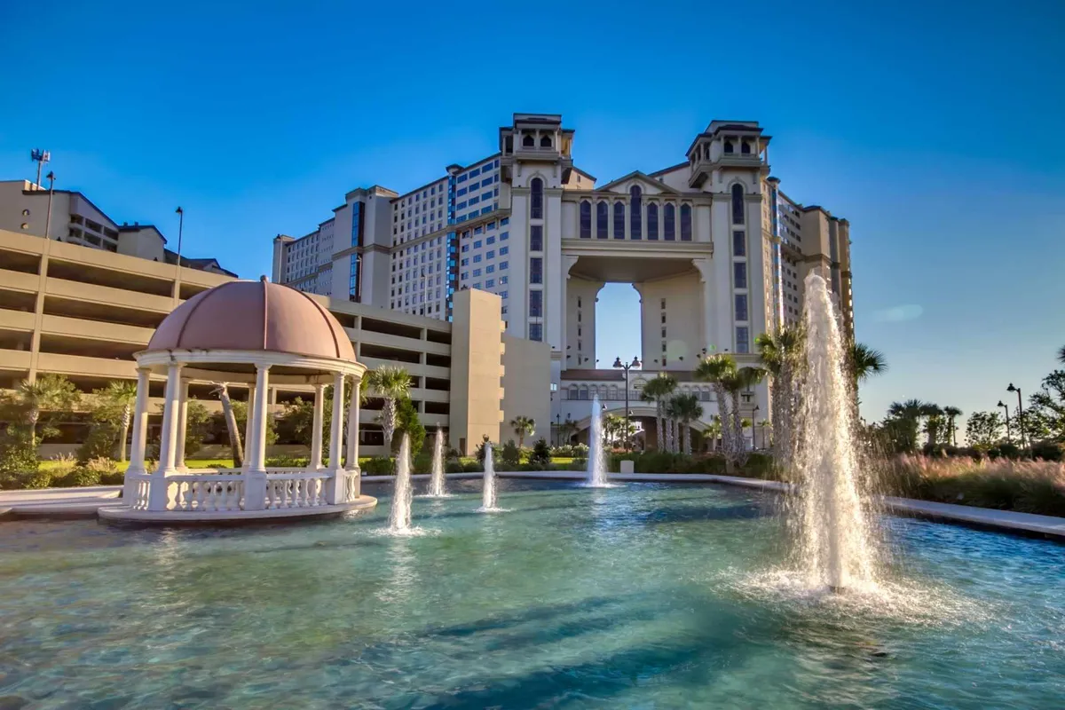 An elegant exterior shot of a grand building with an ornate gazebo and fountains in a reflective pond. The area is well-maintained and designed for social gatherings by the water, giving a sense of both luxury and community.
